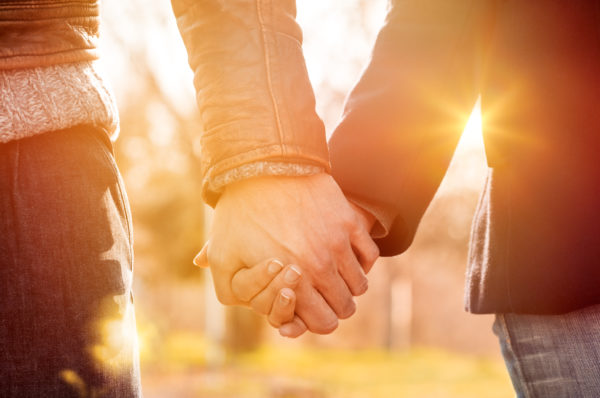 Closeup of loving couple holding hands while walking at sunset